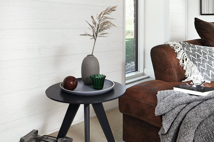 Weiße Wandpaneele mit Struktur, kleiner Beistelltisch mit Deko und braunes Sofa