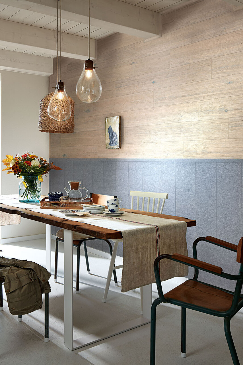 Esstisch mit Blumenvase vor einer Wand an der Filz- und Holzpaneele kombiniert verlegt wurden